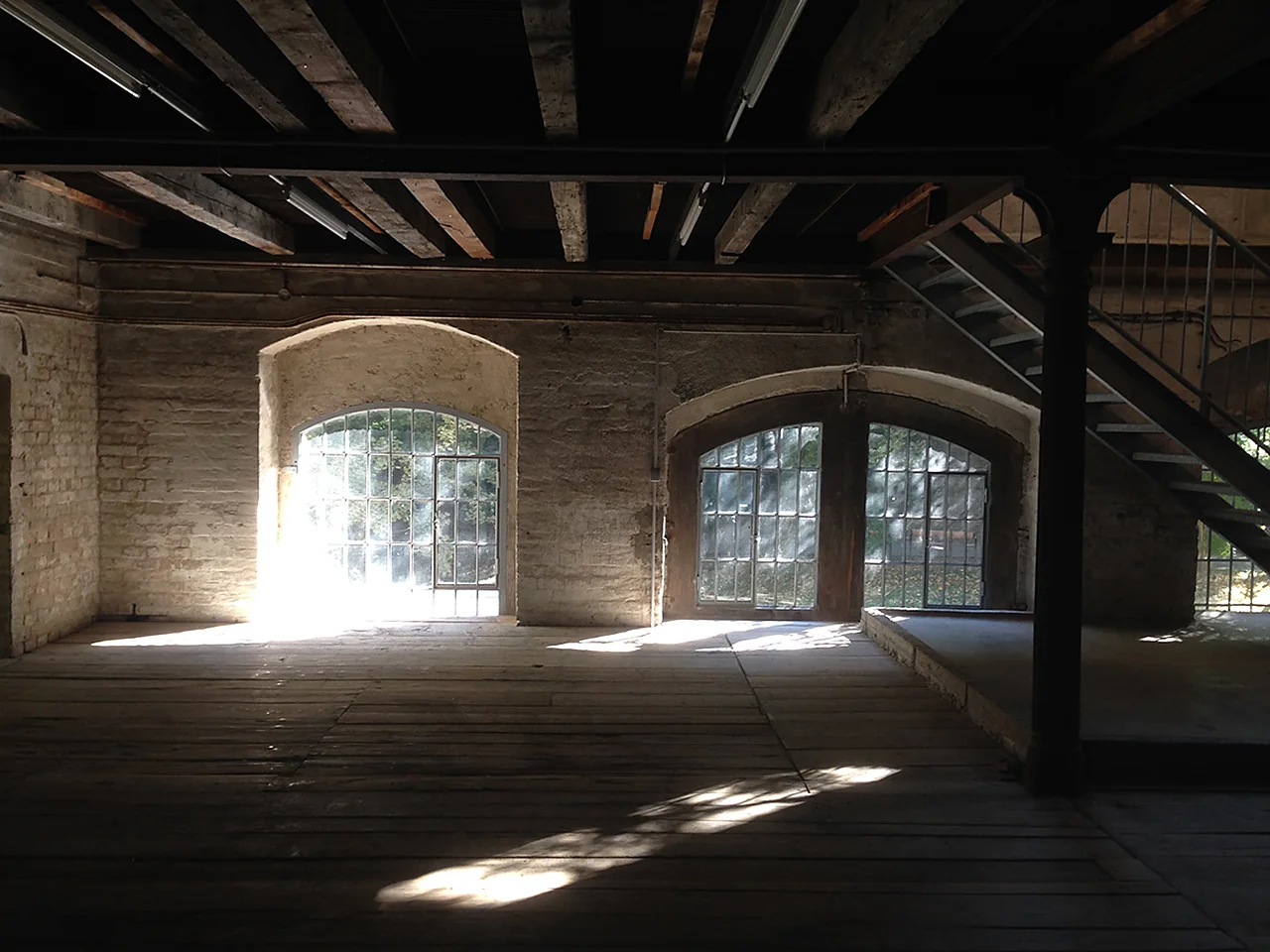Empty room with wooden floor, brick walls and arched windows letting in sunlight