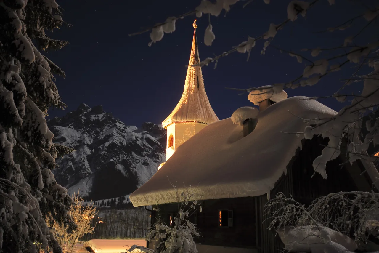 The pilgrimage church of Werfenweng on a snowy winter night, with the mountains behind
